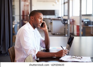 Young Black Man With Laptop On The Phone In An Office