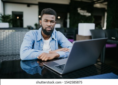 Young Black Man With Laptop Outside A Cafe Looking To Camera