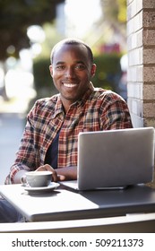 Young Black Man With Laptop Outside A Cafe Looking To Camera