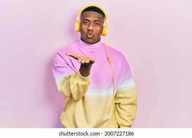 Young Black Man Listening To Music Wearing Headphones Looking At The Camera Blowing A Kiss With Hand On Air Being Lovely And Sexy. Love Expression. 