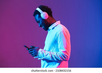 Young black man listening music with headphones and cellphone isolated over purple wall - Shutterstock ID 2108432156