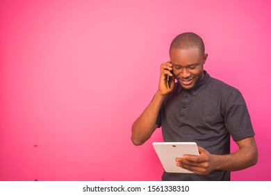 Young black man making a phone call and also pressing his tablet with a smiling face