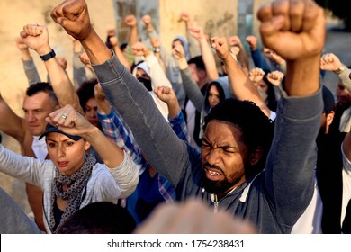 Young black man marching with crowd of people with raised fists on public demonstrations. 