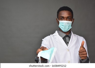 young black man in medical field, wearing a white coat and face mask, offering a face mask
