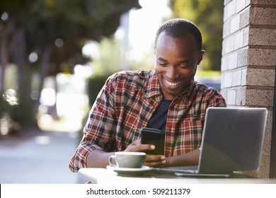 Young black man outside a cafe looking at his smartphone