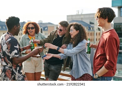 Young Black Man Passing Bottle Of Beer And Cocktail To Guy And Girl During Rooftop Party Or Gathering In Outdoor Cafe On Weekend