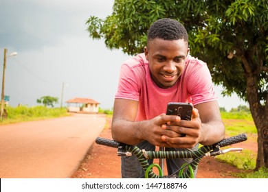 Young Black Man Resting On His Bicycle Smiling While Using His Phone