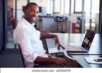 Young Black Man Sitting At Desk In Office Smiling To Camera