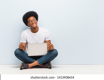 Young black man sitting on the floor with a laptop dreaming of achieving goals and purposes