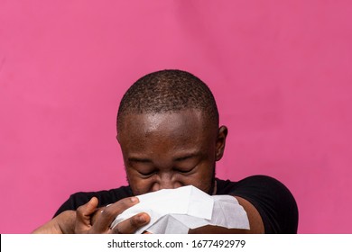 Young Black Man Sneezing Into A Napkin On His Elbows