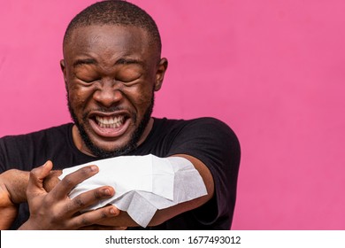 Young Black Man Sneezing Into A Napkin On His Elbows