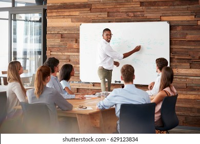 Young Black Man Stands At Whiteboard Addressing Team At Meeting