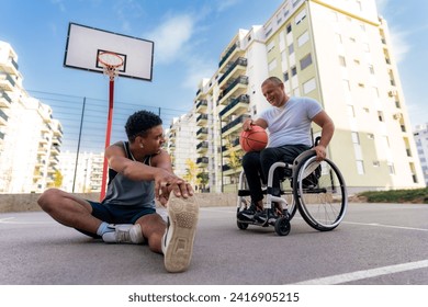 A young black man stretches as he has a conversation with an older man in wheelchair before or after a friendly one-on-one game of basketball - Powered by Shutterstock