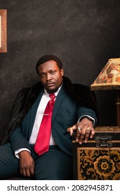 Young Black Man in Suit and Fur Coat Sitting by a Vintage Lamp and Old Chest in the Style of a Renaissance Painting