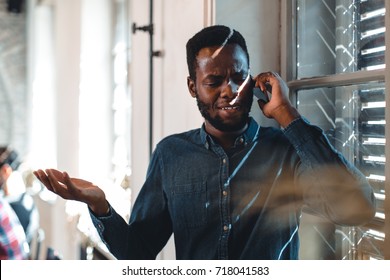 Young Black Man Talking On The Phone Next To The Window