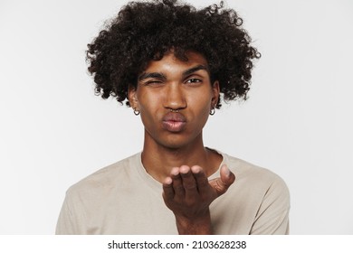 Young black man in t-shirt winking and blowing air kiss at camera isolated over white background