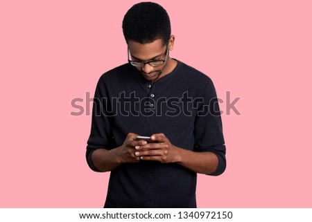 Young black man uses mobile phone, checking social media on smartphone. Handsome female wears casual jumper, holds his gadget, looks down, finds information in Internet. People and technology concept.