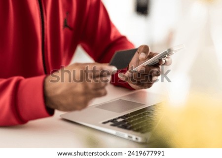 Young black man using his mobile phone to enter information from his card