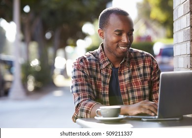 Young Black Man Using A Laptop Computer Outside A Cafe