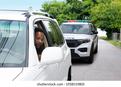 Young Black Man With A Very Worried Look On His Face Is Looking At The Police Car That Has Pulled Him Over In His Rearview Mirror Reflecting The Problems Between Citizens And Some Police Departments.