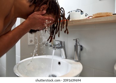 Young Black Man Washing His Face With Water In Wash Basin In Bathroom At Home At Morning Time. Concept Of Domestic Lifestyle. Idea Of Face Care. Cropped Image Of Bearded Dark Haired Guy