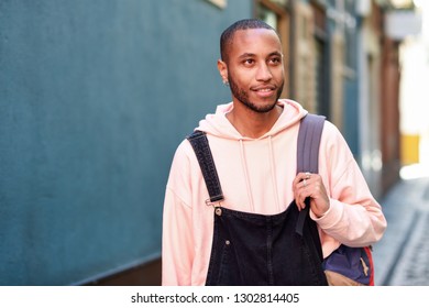 Young Black Man Wearing Casual Clothes Walking Smiling Down The Street. Millennial African Guy With Bib Pants Outdoors