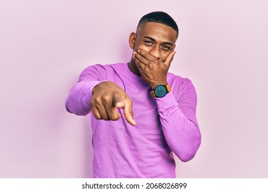 Young Black Man Wearing Casual Pink Sweater Laughing At You, Pointing Finger To The Camera With Hand Over Mouth, Shame Expression 