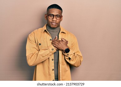 Young Black Man Wearing Casual Clothes And Glasses Smiling With Hands On Chest With Closed Eyes And Grateful Gesture On Face. Health Concept. 