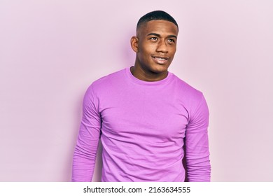 Young Black Man Wearing Casual Pink Sweater Looking Away To Side With Smile On Face, Natural Expression. Laughing Confident. 