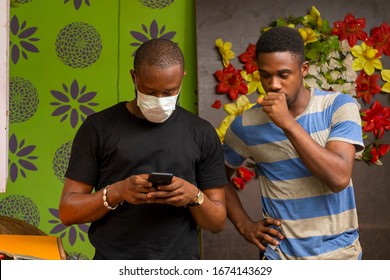 Young Black Man Wearing A Face Mask And Using His Phone, Someone Coughing Close To Him