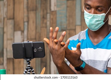 Young Black Man Wearing Face Mask And Using Hand Sanitizer, Making A Video Blog With Mobile Phone