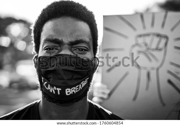 Young\
black man wearing face mask during equal rights protest - Concept\
of demonstrators on road for Black Lives Matter and I Can\'t Breathe\
campaign - Focus on eyes - Black and white\
editing