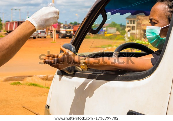 young black man wearing a\
gloves, applying hand sanitizer to the hand of a black woman\
driving a car