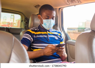 young black man wearing a nose mask, sitting in the car and pressing his smartphone
