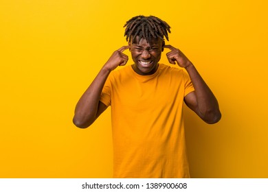 Young black man wearing rastas over yellow background covering ears with his hands. - Shutterstock ID 1389900608