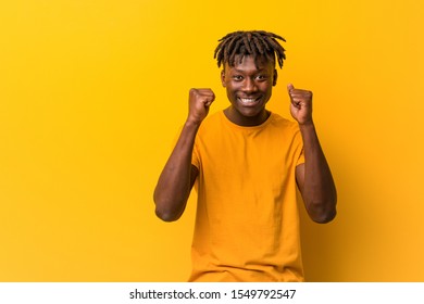 Young black man wearing rastas over yellow background raising fist, feeling happy and successful. Victory concept. - Shutterstock ID 1549792547