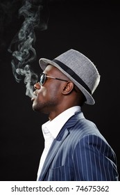 Young Black Man Wearing Suit And Hat And Sunglasses. Smoking A Cigarette.