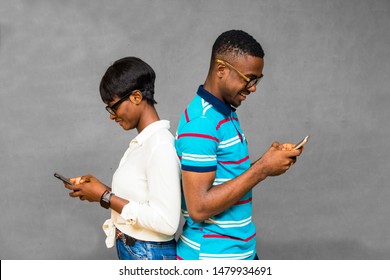 Young Black Man And Woman Standing Together Back To Back, Using Their Phones And Smiling