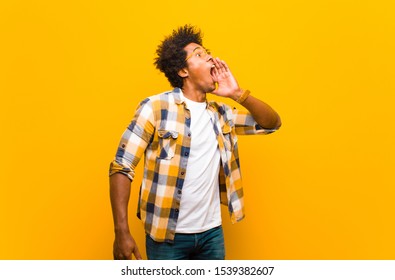 Young Black Man Yelling Loudly And Angrily To Copy Space On The Side, With Hand Next To Mouth Against Orange Wall