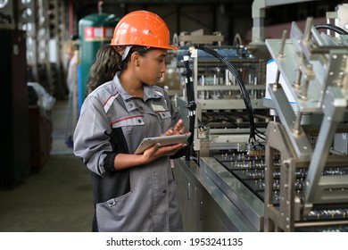 A young black manufacturing worker controls an assembly line in a factory, making notes on a tablet. Young woman in hard hat watches the work process - Powered by Shutterstock