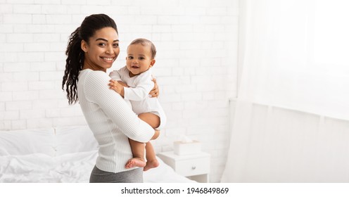 Young Black Mom Holding Baby Toddler, Hugging Carrying Adorable Little Son Posing Standing Indoors. Child Care, Motherhood And Maternity Leave Concept. Panorama, Empty Space For Text