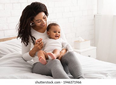 Young Black Mom Holding Little Toddler Baby Playing With Son Enjoying Motherhood In Bedroom At Home. African American Mother Caring For Child Bonding With Her Kid Indoors. Maternity Leave Concept