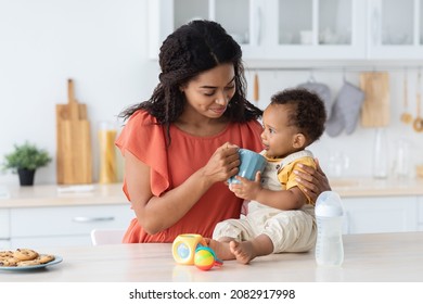 Young Black Mother Giving Try Drink From Her Cup To Infant Baby While They Spending Time Together In Kitchen At Home, Cute Little Toddler Boy Enjoying Mom's Tea, Licking Lips With Pleasure, Closeup