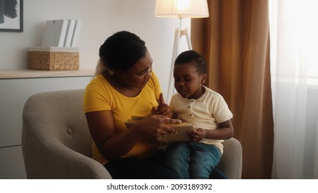 Young Black Mother And Little Son Reading Book Together While Sitting In Chair At Home, African American Nanny Making Educational Activities With Preschooler Male Child, Slow Motion Footage