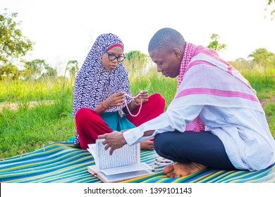 Young Black Muslim Man Reading The Quran And Muslim Lady Praying The Tasbih Outside