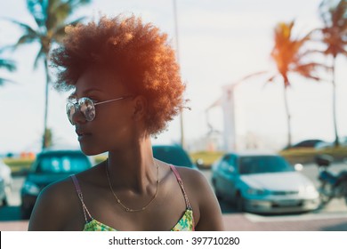 Young Black Pretty Attractive Female With Curly Hair Looking Around, Walking On Street Of Tropical City With Palm Trees And Parked Cars, Sunny Bright Summer Day, Vintage Color Filter