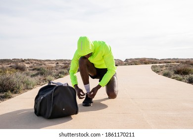 Young Black Runner With Bag And Yellow Rain Jacket Ties His Laces And Gets Ready To Train.