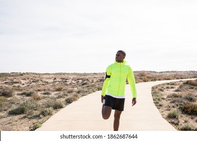 Young Black Runner In A Yellow Rain Jacket Stretching His Legs Before Or After Training.