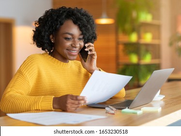 Young black smiling businesswoman talking to colleagues by phone, working with laptop at cafe - Shutterstock ID 1653230518