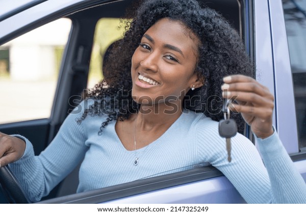 A young black\
smiling woman show her key\
car